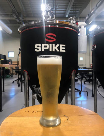 Glass of Belgian Wit beer in front of a Spike Brewing homebrew system.