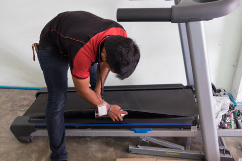 Man maintaining a treadmill by adding lubrication to the belt