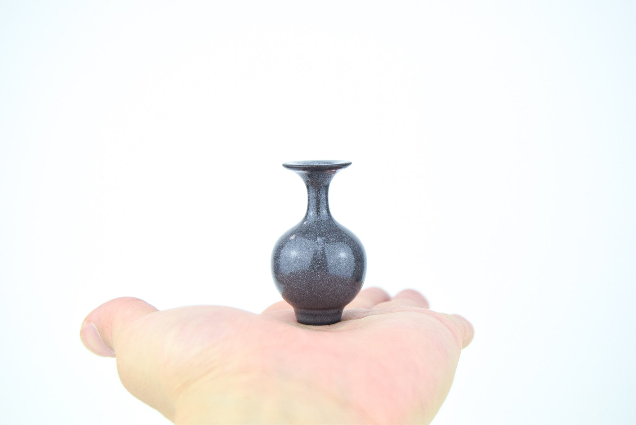 A tiny exquisite ceramic vase sat on the maker's hand.