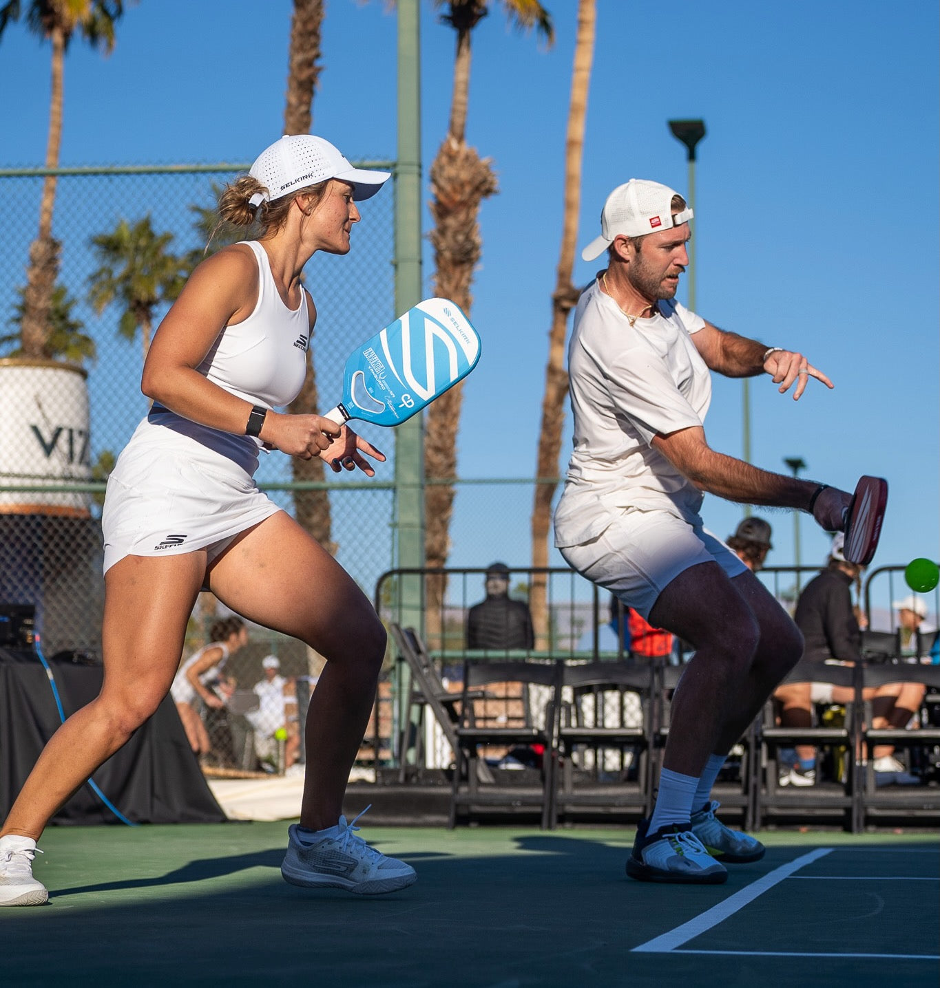 Professional pickleball players Catherine Parenteau and Jack Sock stack during a match. Jack is serving from the right side of the court while Catherine stands to the right of him, and both are ready to slide over as soon as he serves.