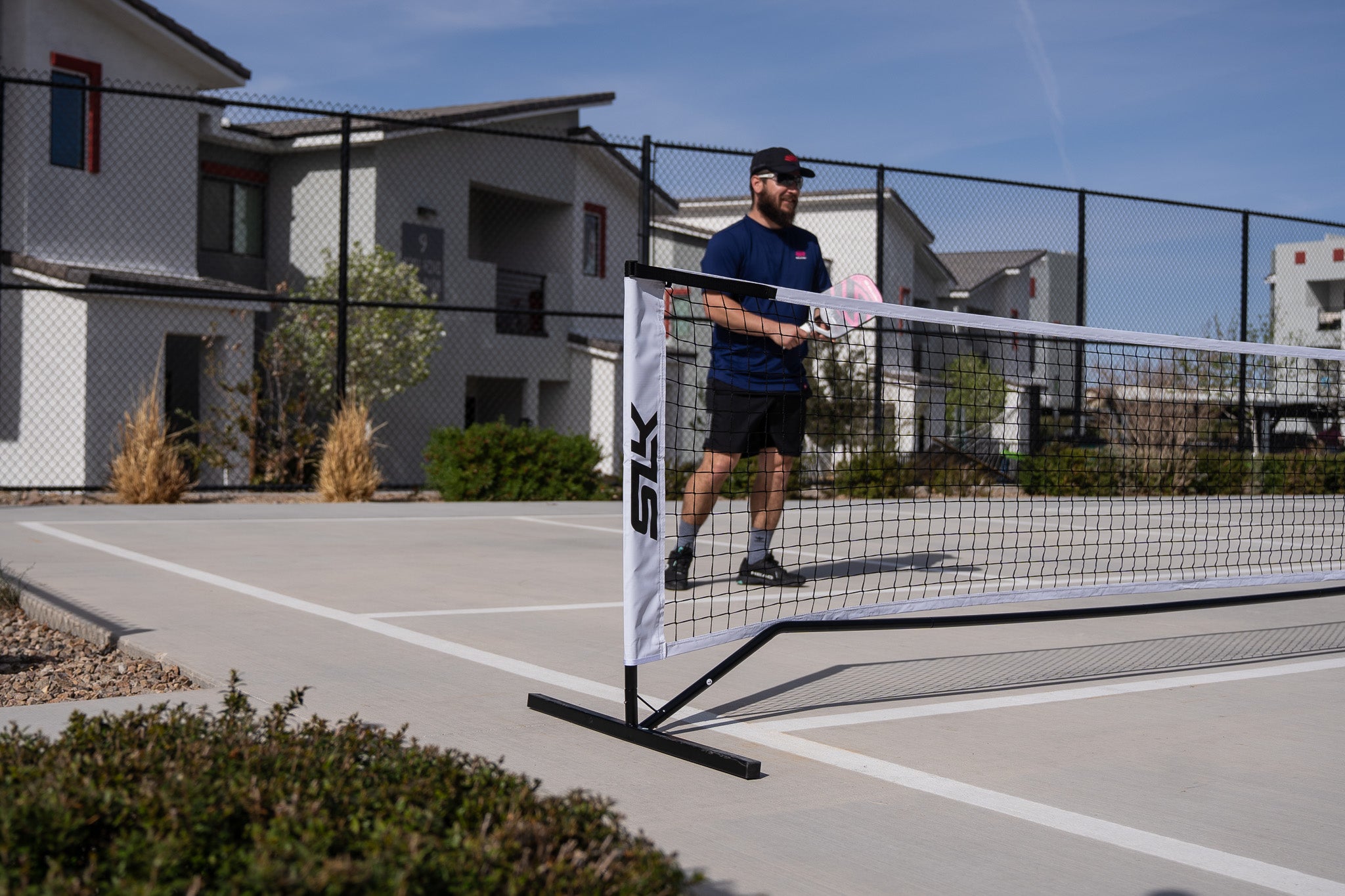 A man stands on a pickleball court behind a temporary pickleball net. He is ready to hit a volley.