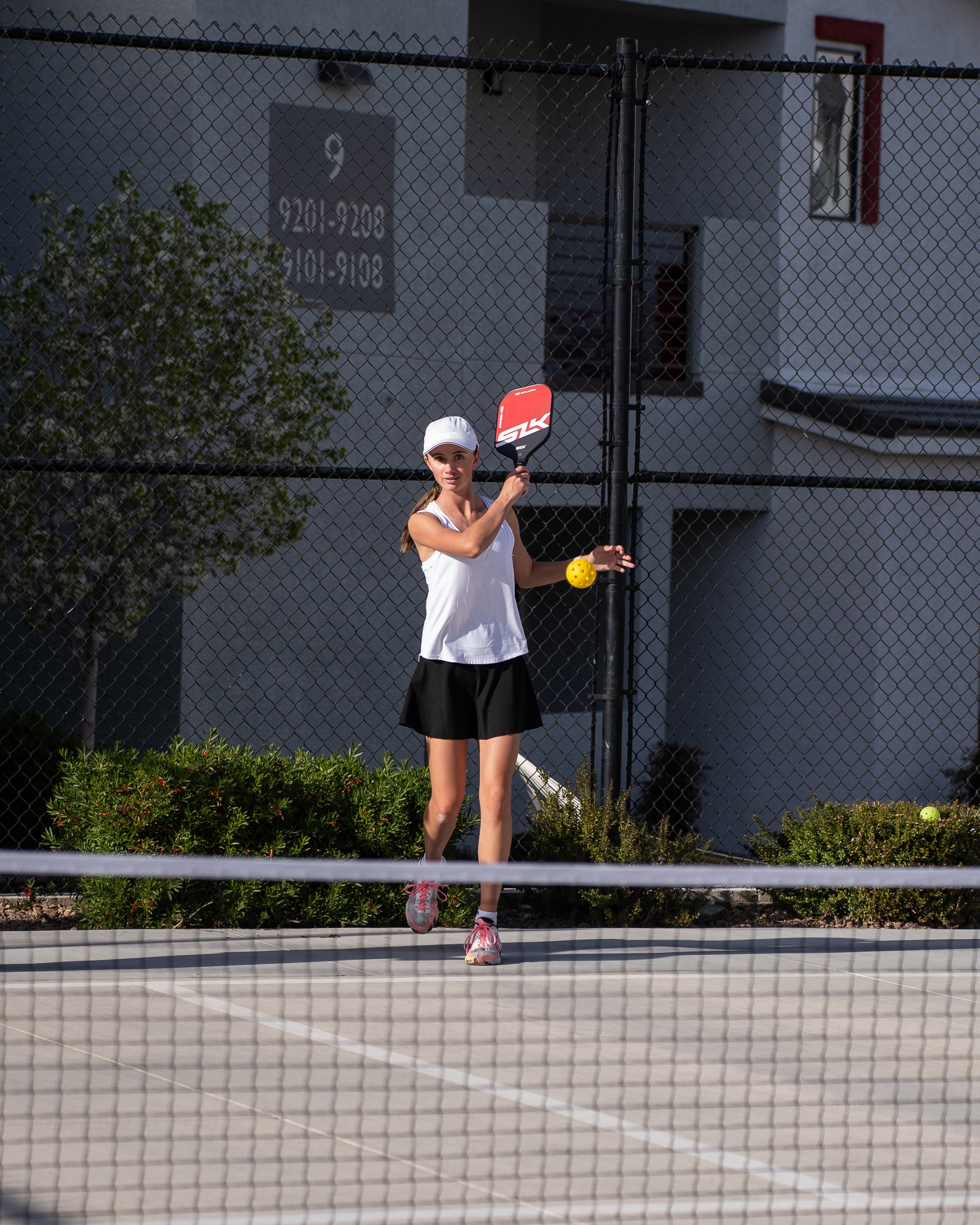 A woman serves a pickleball across a pickleball net.