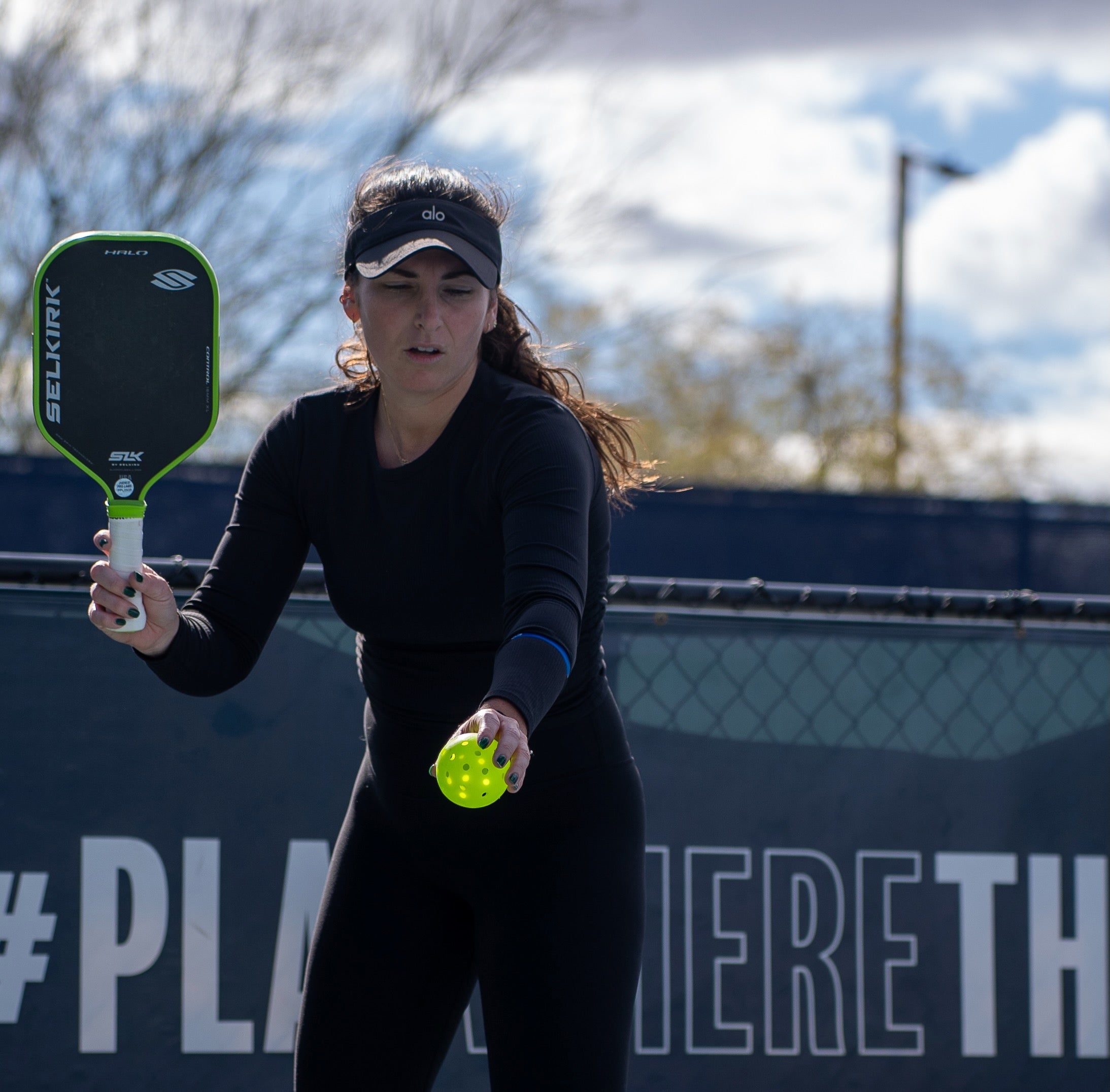 Professional pickleball player Rachel Rohrabacher prepares to serve the pickleball. She holds her SLK Halo high and a pickleball out in front of her.