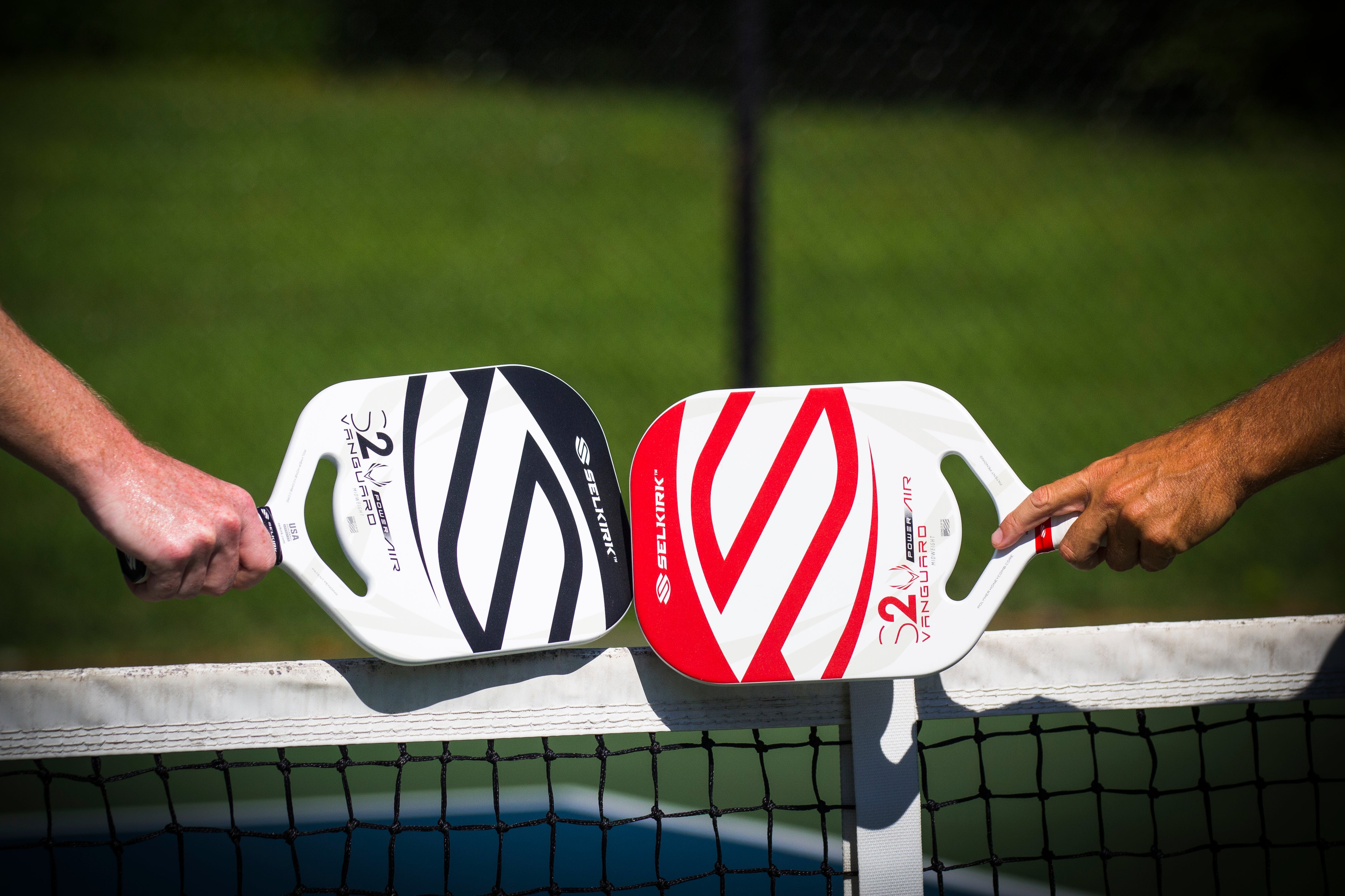 Two players tap their Selkirk Vanguard Power Air paddles over the net after finishing a game.