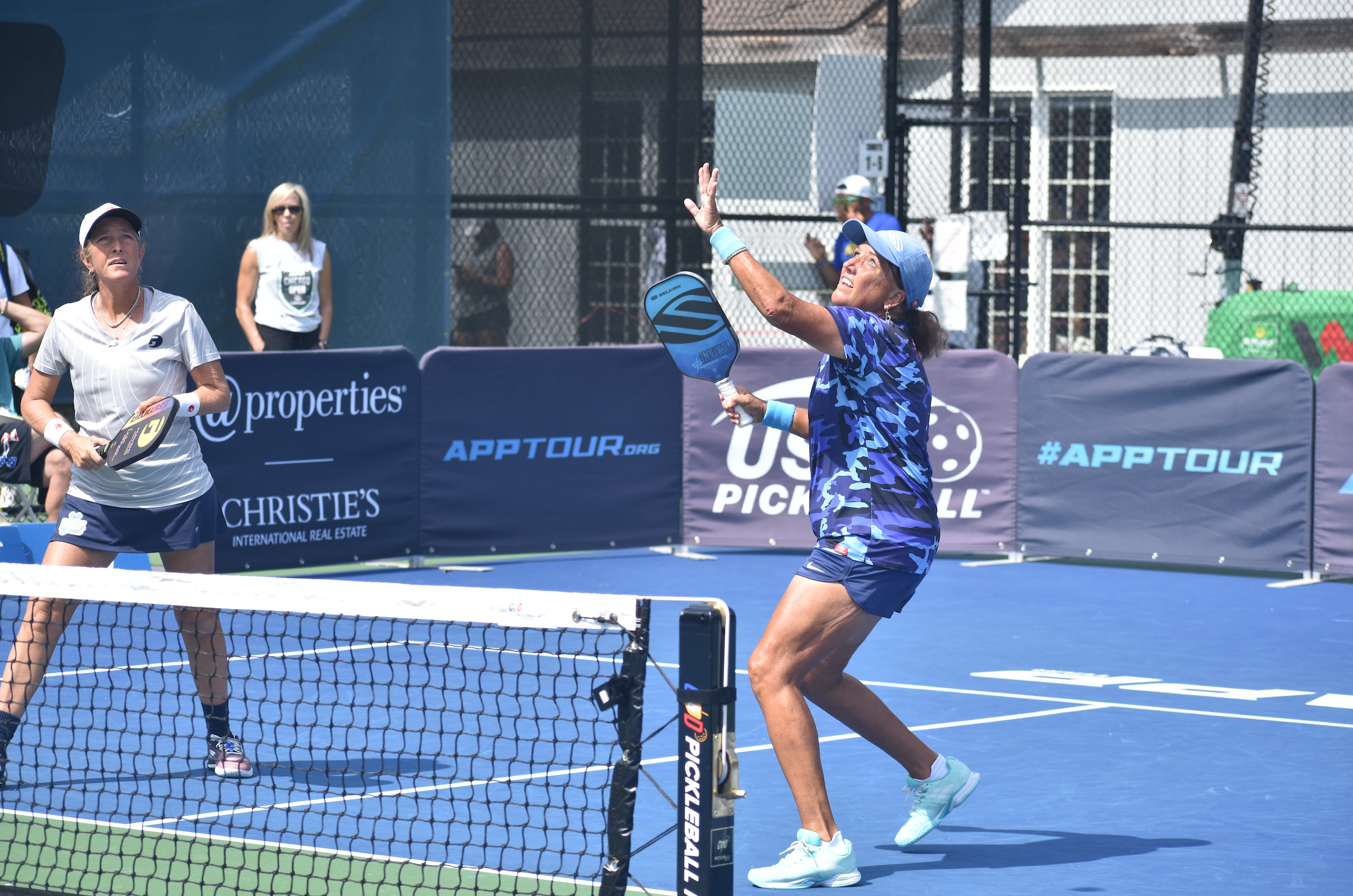 Professional pickleball player Linda Thompson attempts to hit a putaway shot on the pickleball court, twisting her neck and upper back to hit it.