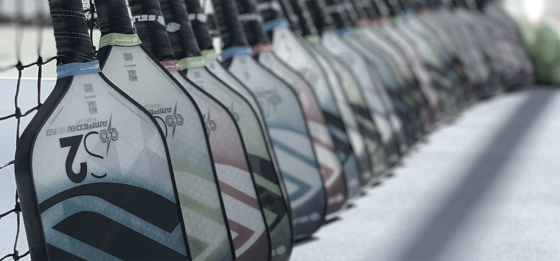 Selkirk pickleball paddles lined up against a net.