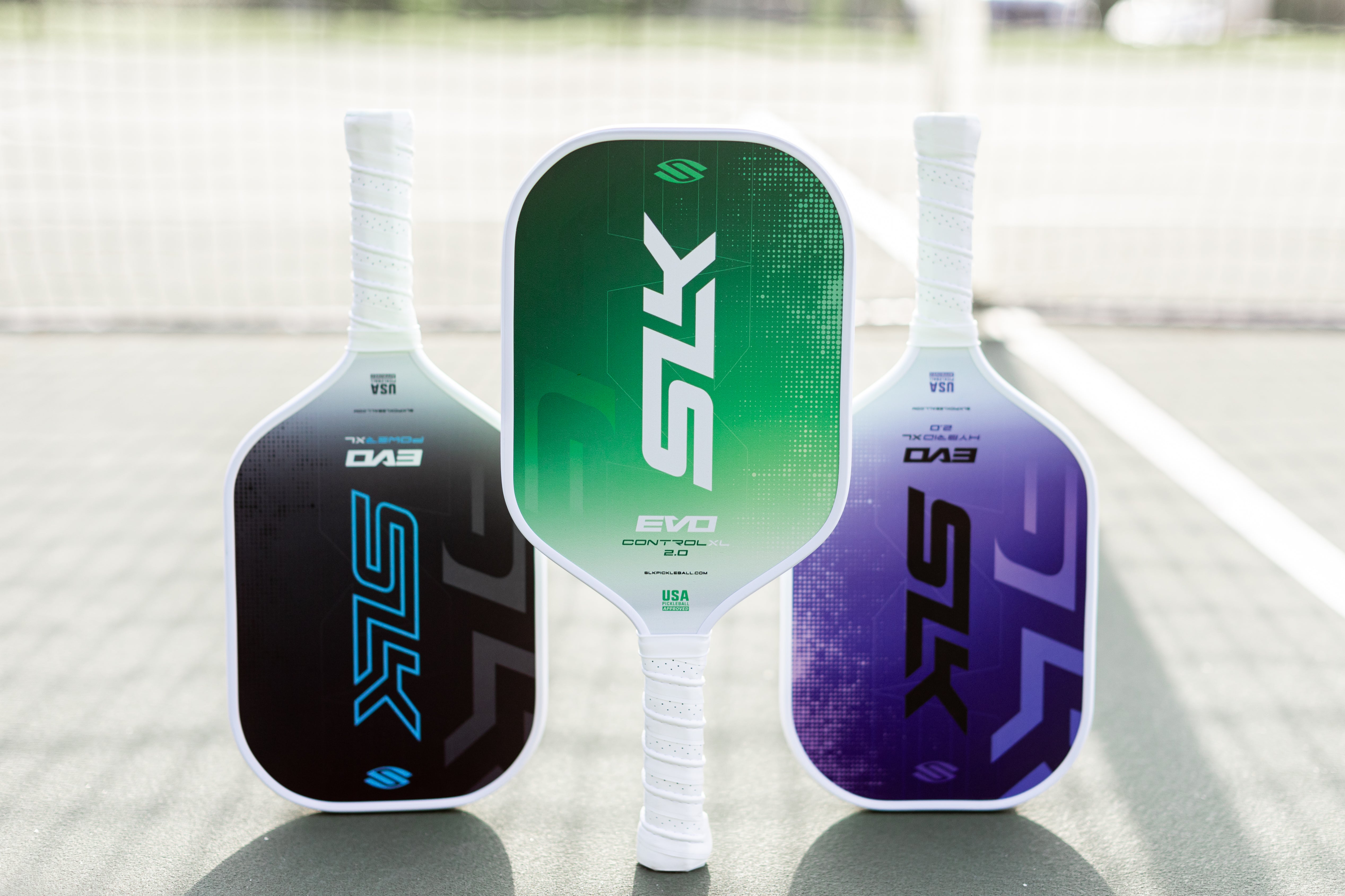 Three Selkirk Evo paddles stand upright in a line on a pickleball court.