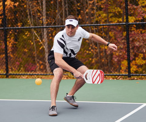 A man plays pickleball and squats awkwardly to hit a shot, putting strain on his knees.