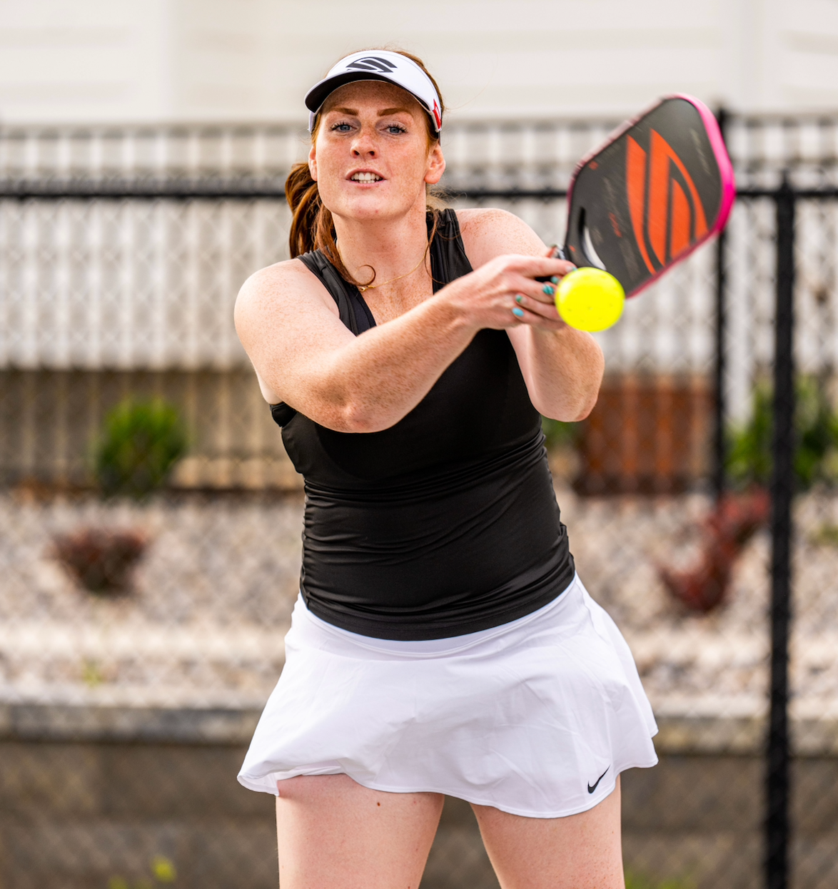 Selkirk Emerging Pro Brooke Bromley hits a two-handed backhand volley with her Project 002 paddle. She wears a white Selkirk visor, a black tank top and a white Nike skirt.