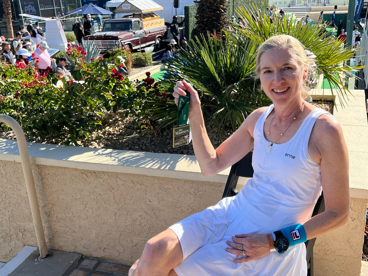 Lynn Beck relaxes near a pickleball court. She holds up her PPA Masters medal as she smiles at the camera.