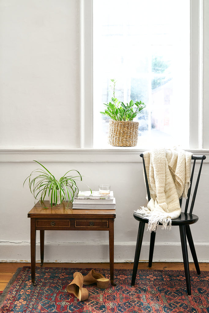 A vintage rug is styled with an antique table and a black chair.