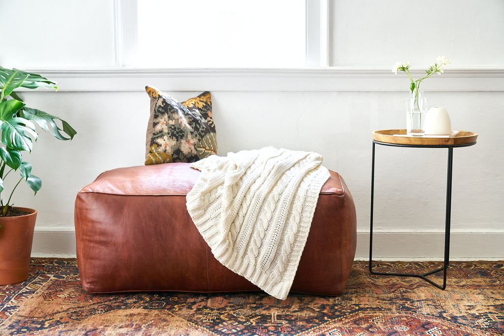 A vintage rug is styled with a large leather pouf.