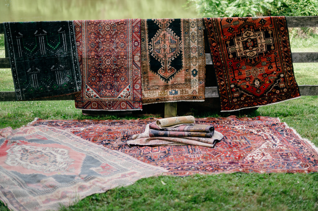Colorful vintage rugs hang on a rustic fence.