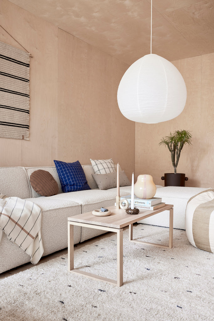 scandi style living room with white sofa, wood paneled wall, striped wall hanging abd and white paper lantern