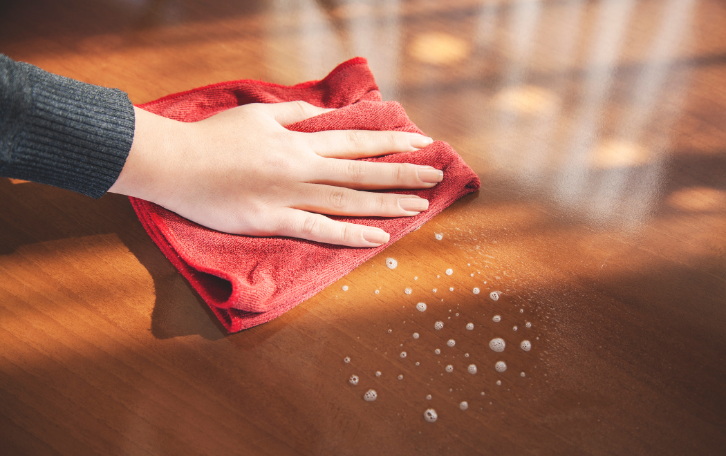 Person cleaning wooden table with red cloth