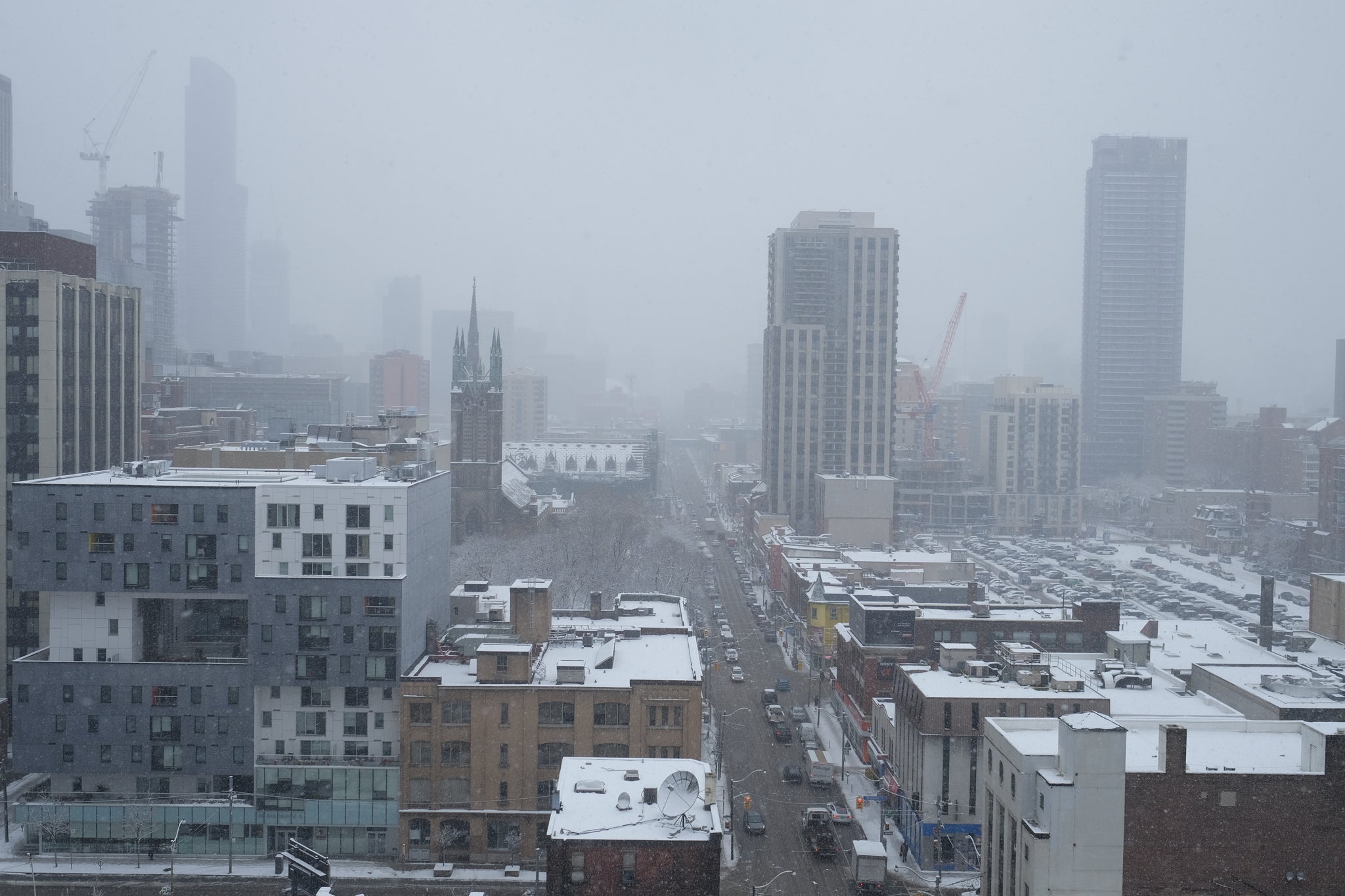 A picture showing the roads in the winter with snow falling and bicycles and cars commuting.