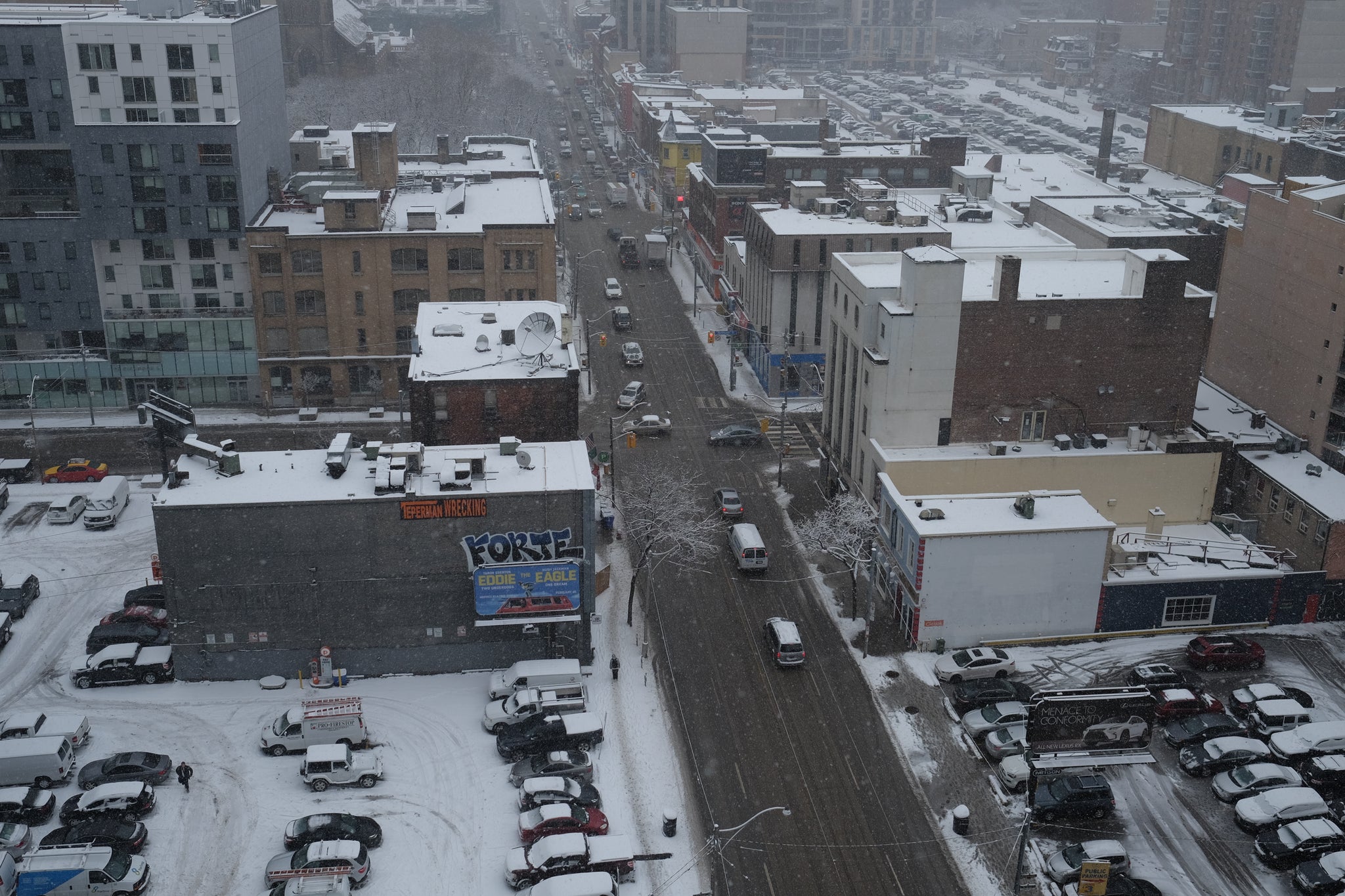 The picture shows the streets of Toronto covered with snow and cars and bicycles moving through the snow
