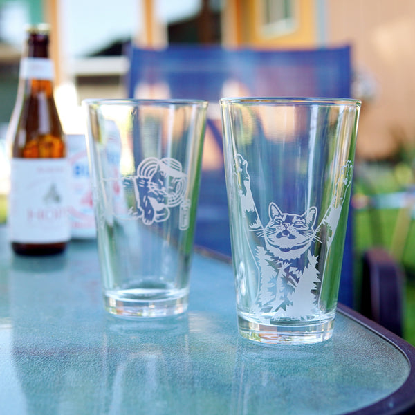 etched pint glasses with cats on them, sitting on a patio table on a sunny day