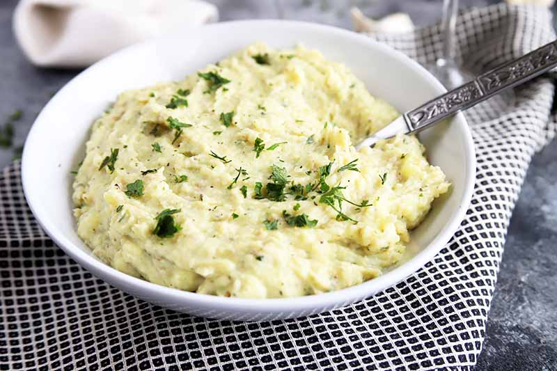 A bowl of mashed potato sprinkled with chopped herbs.