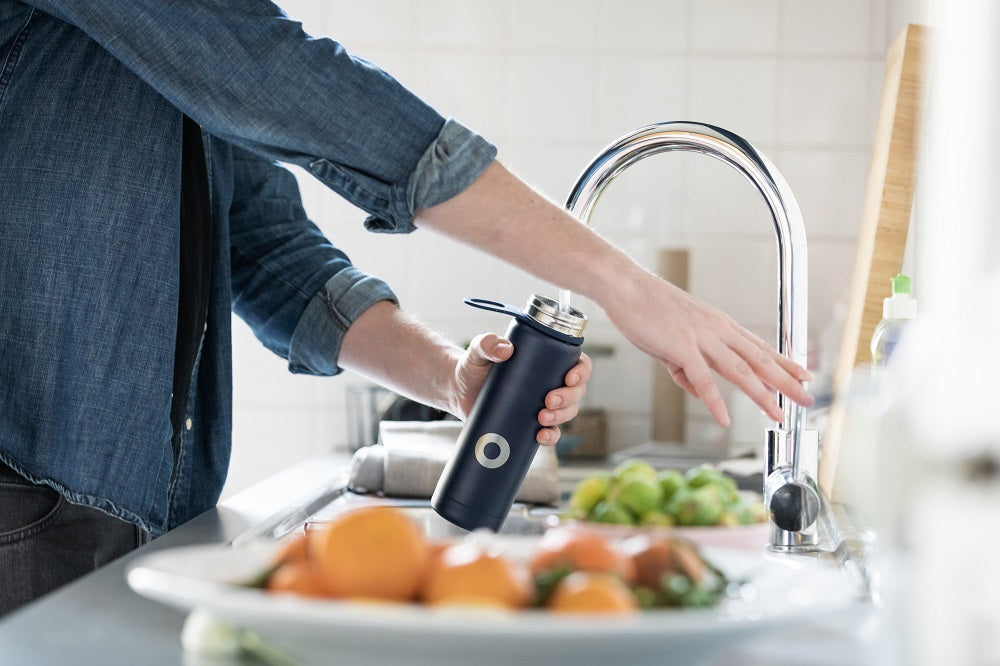 Person filling reusable water bottle with tap water.