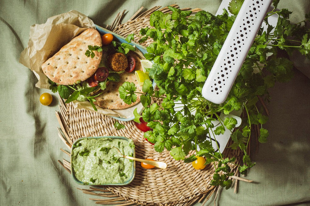 Pita pockets on a table alongside fresh greens growing in a smart garden.