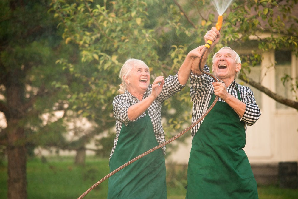 Elderly couple laughing and having fun with a hosepipe.