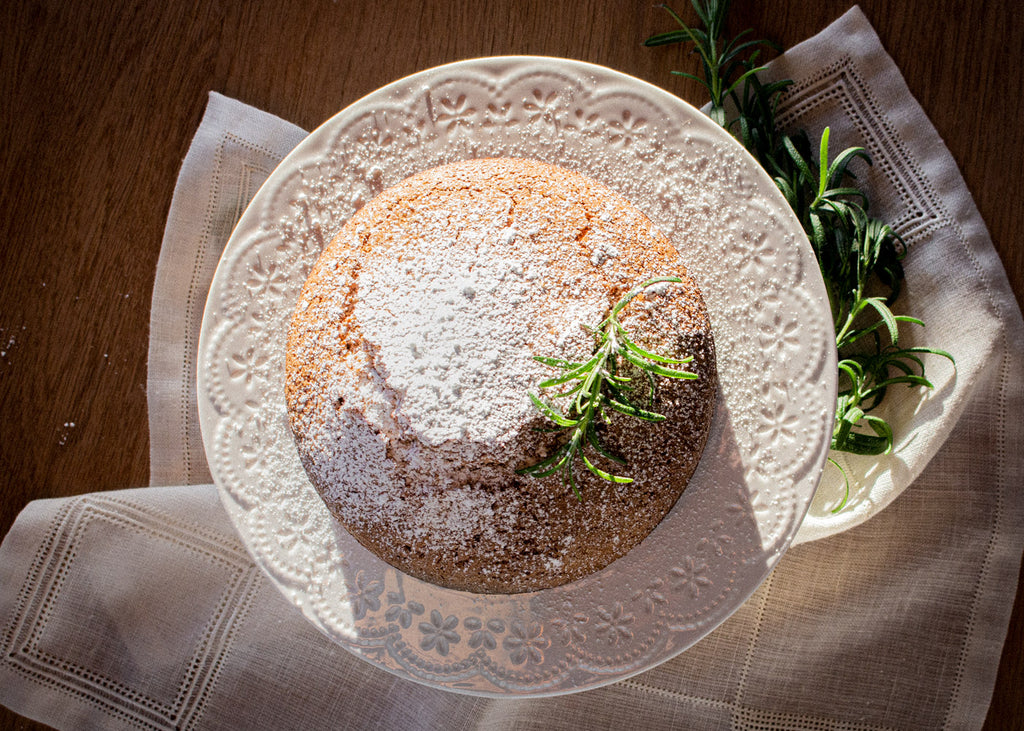 Cake topped with powdered sugar and fresh rosemary on a wooden table.