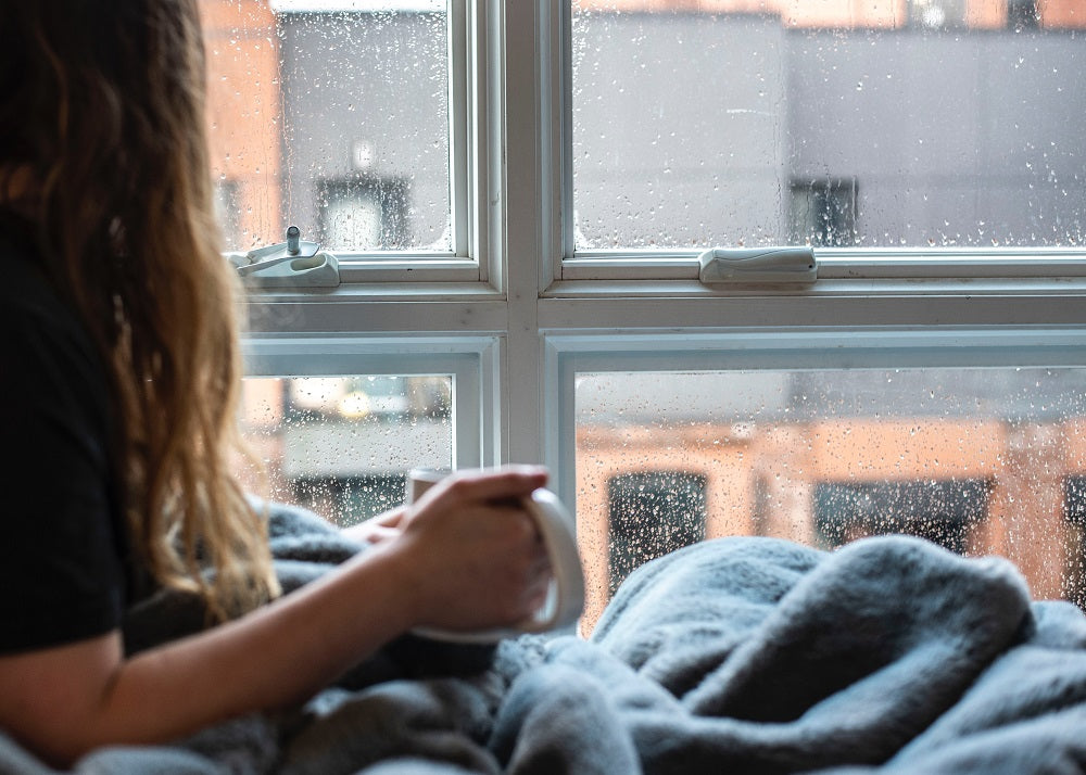 Woman holding a mug and looking out of the window during winter.