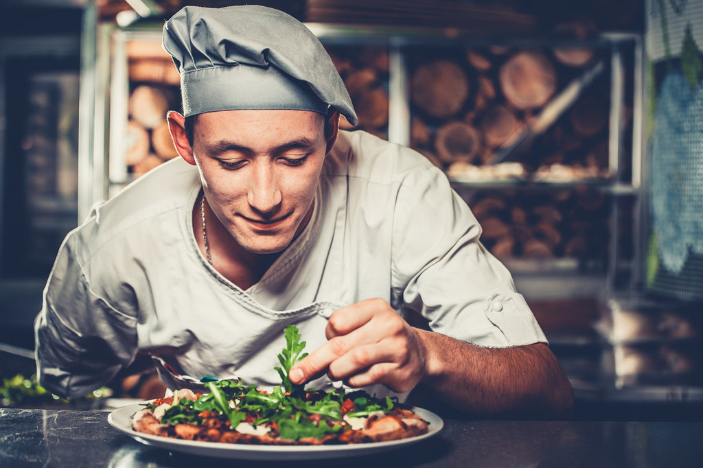 Smiling chef topping a pizza with herbs.