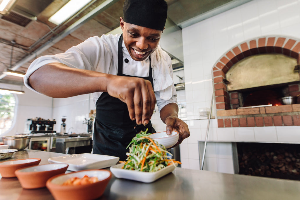 Smiling chef seasoning a salad in a kitchen.