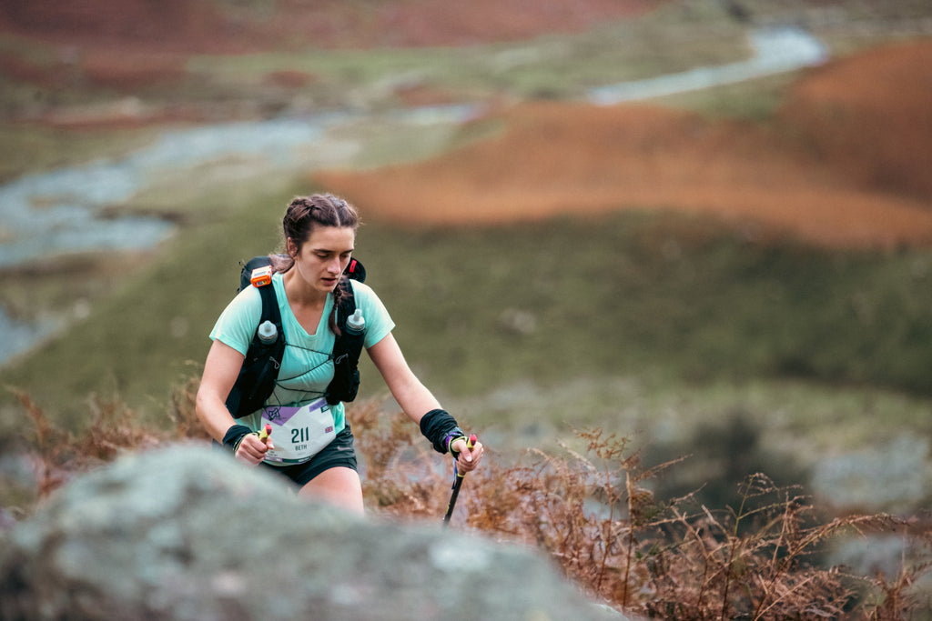 A female trail runner using running poles climbs a steep ascent in the Lake District