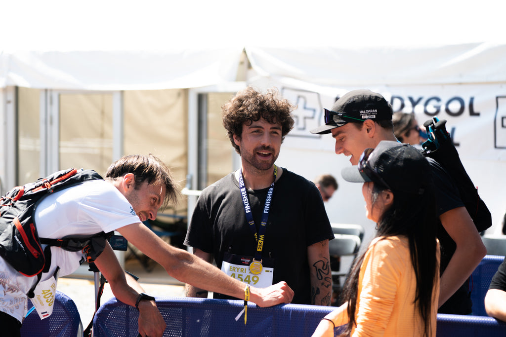 An ultra runner leans over on a barrier whilst talking to friends after an ultra distance event in hot conditions