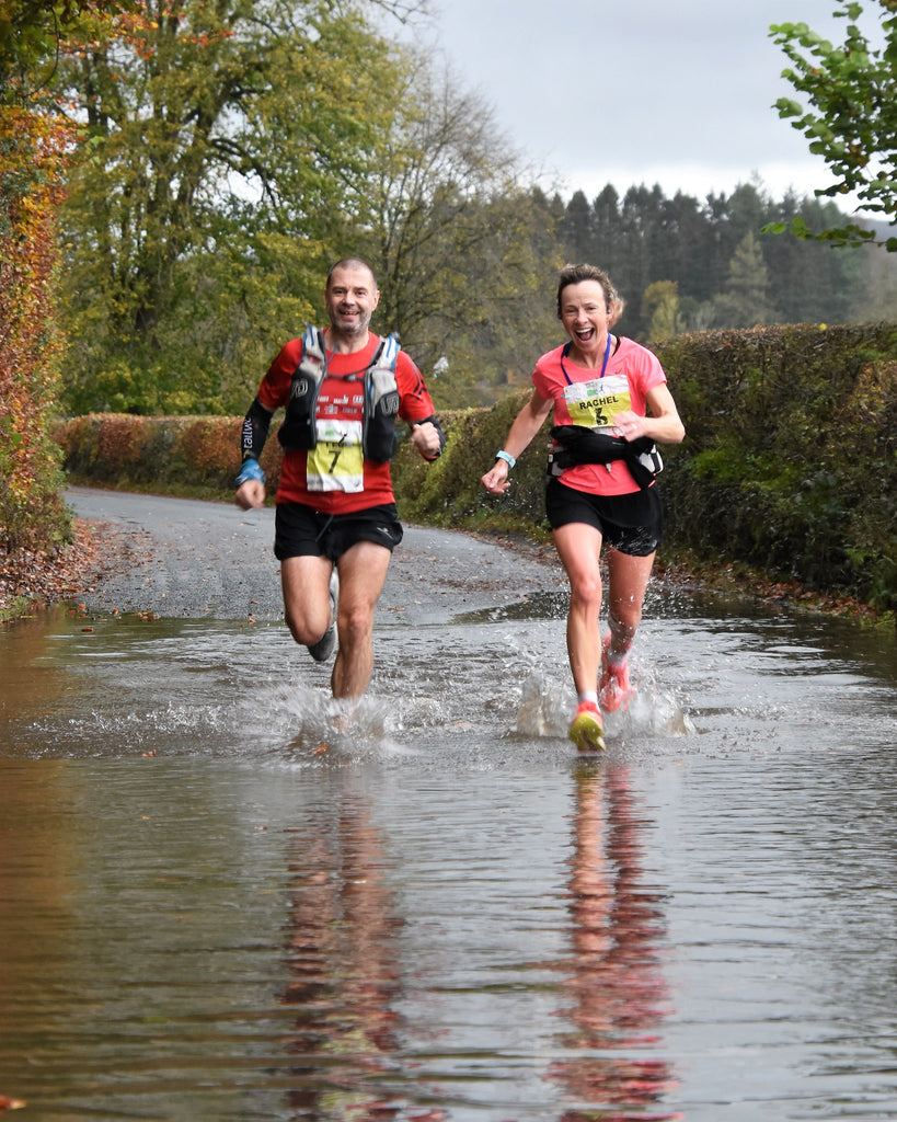 Two smiling runners splash through a puddle during the Brathay 10in10 challenge 2020