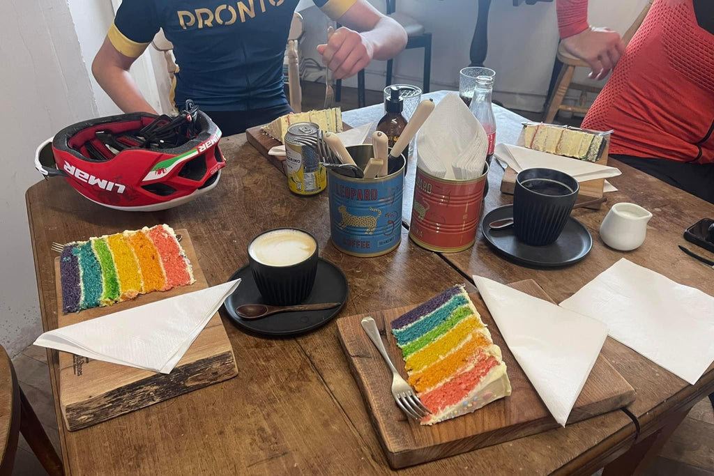 Three cyclists each with a slice of rainbow cake during a cafe stop on a ride around wiltshire