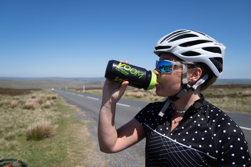 A cyclist taking a drink from a VOOM bottle beside the road they've cycled along.