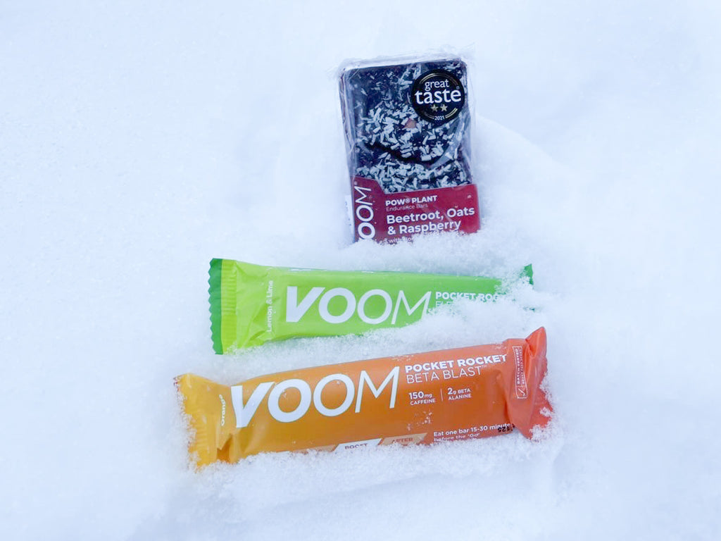 Two VOOM Pocket Rocket bars and a VOOM Pow Plant Beetroot Endurance Bar laying in the snow as they were used in the arctic.