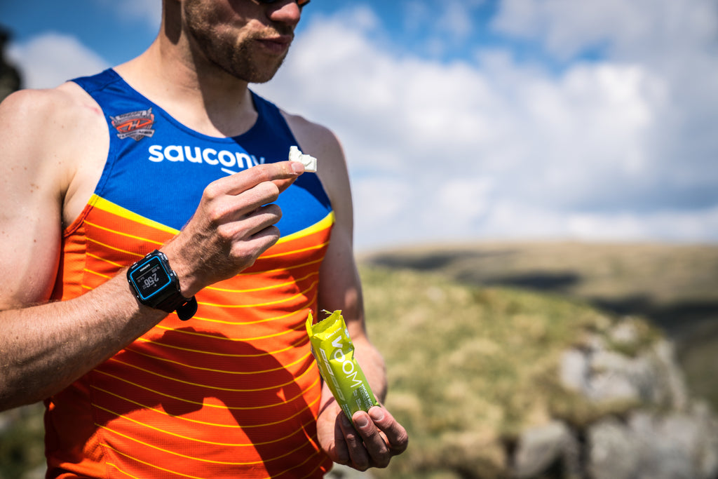 A male runner holds an energy bar and one VOOM Pocket Rocket chunk whilst out running