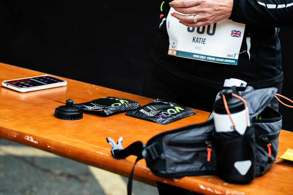 Two VOOM Fusion Fuel sachets on a table as a runner mixes carbohydrate drinks up for an ultra running event.