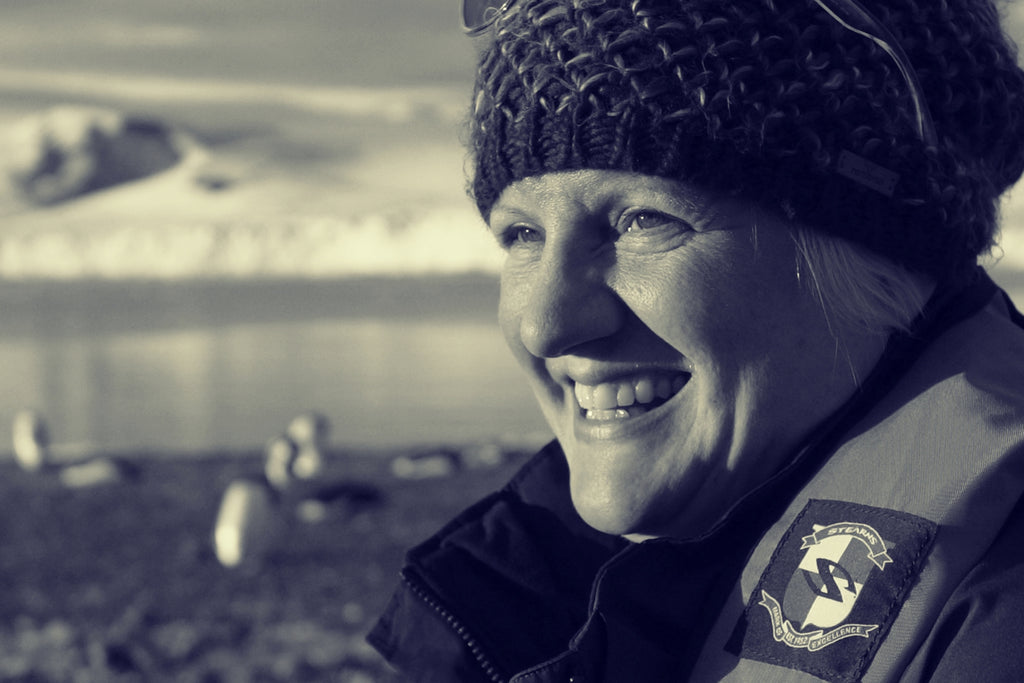 Ice swimmer Cath Pendleton stands beside the icy sea with a wolly hat on.