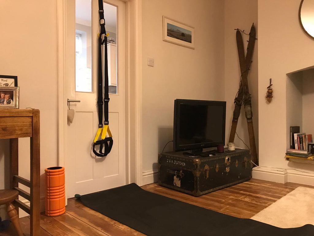 A TRX suspension trainer and foam roller set out with a fitness mat for home training in someone's living room