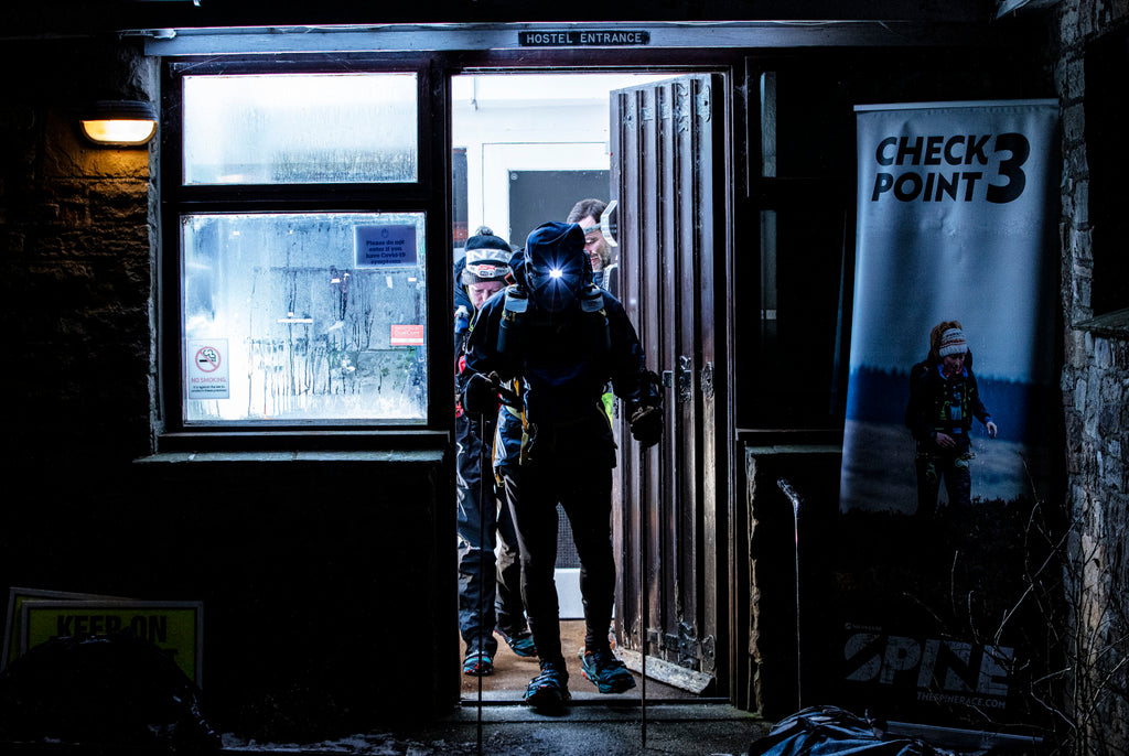 A silhouetted runner departs a brightly lit doorway into the darkness after the Langden Beck Youth Hostel checkpoint during spine race