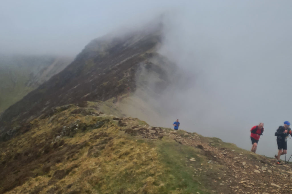 Bad weather closes in on three ell runners on a mountain ridge in the Lake District