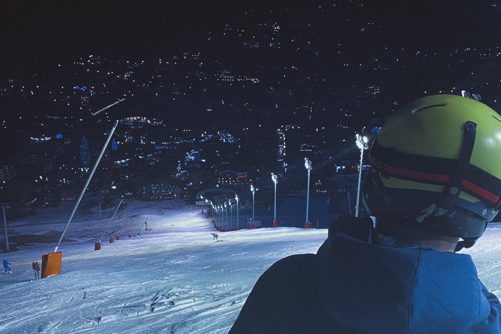 A skiier looking down the mountain during a night skiing session with the lights of a town below