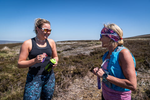Two female runners enjoying eating an energy bar on a moorland path
