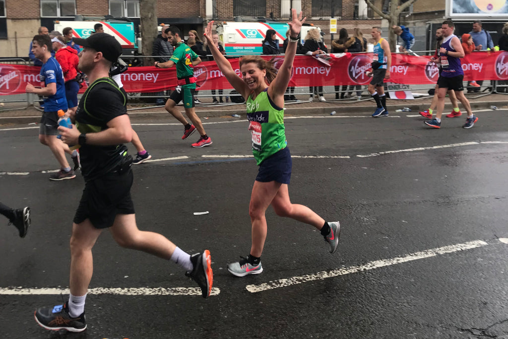 A female marathon runner waves to family whilst running past in the rain