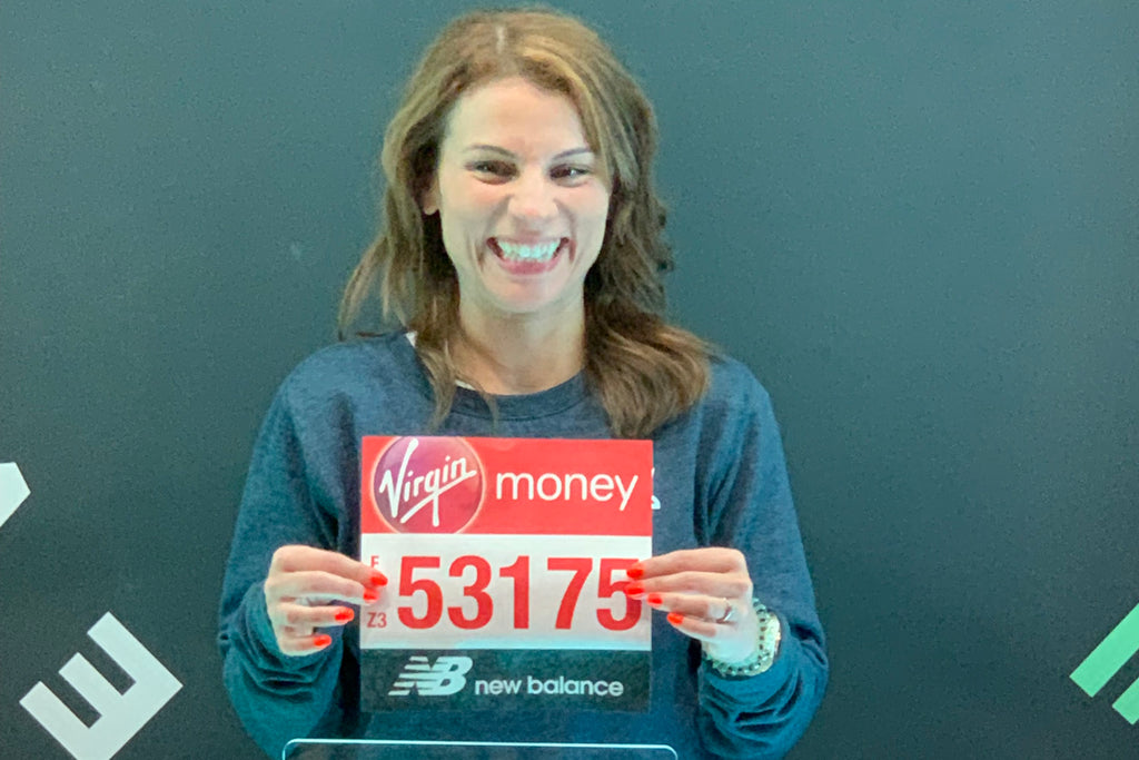 Ruth Bennett holds up her London Marathon bib number with a big smile on her face