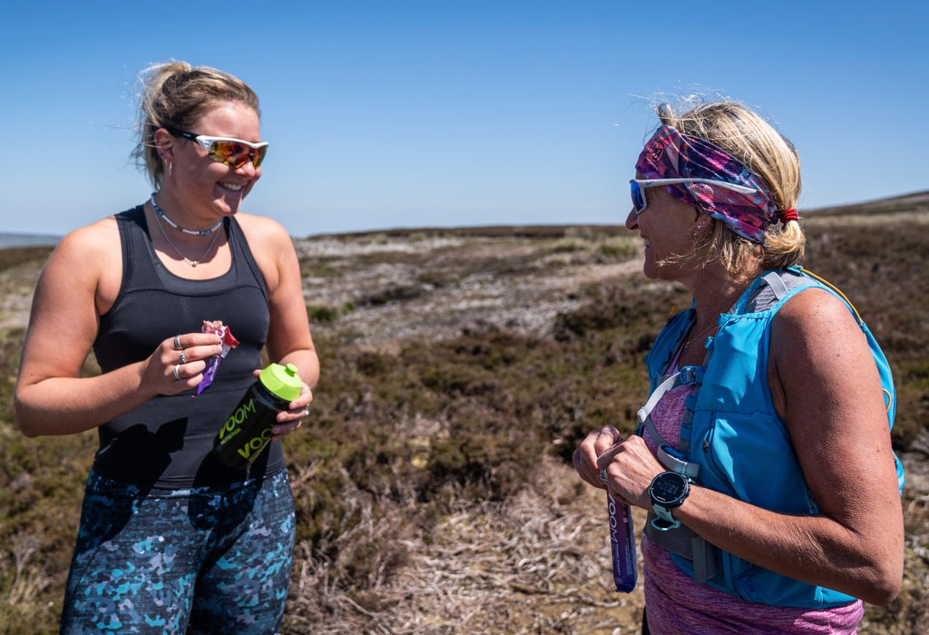 Two female runners enjoying eating an energy bar on a moorland path