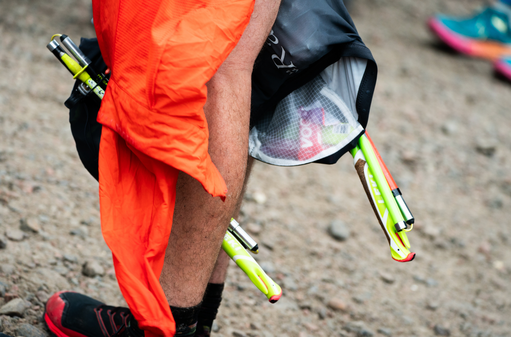 A trail runners pack hangs open down beside their legs showing VOOM energy bars and Leki running poles inside.