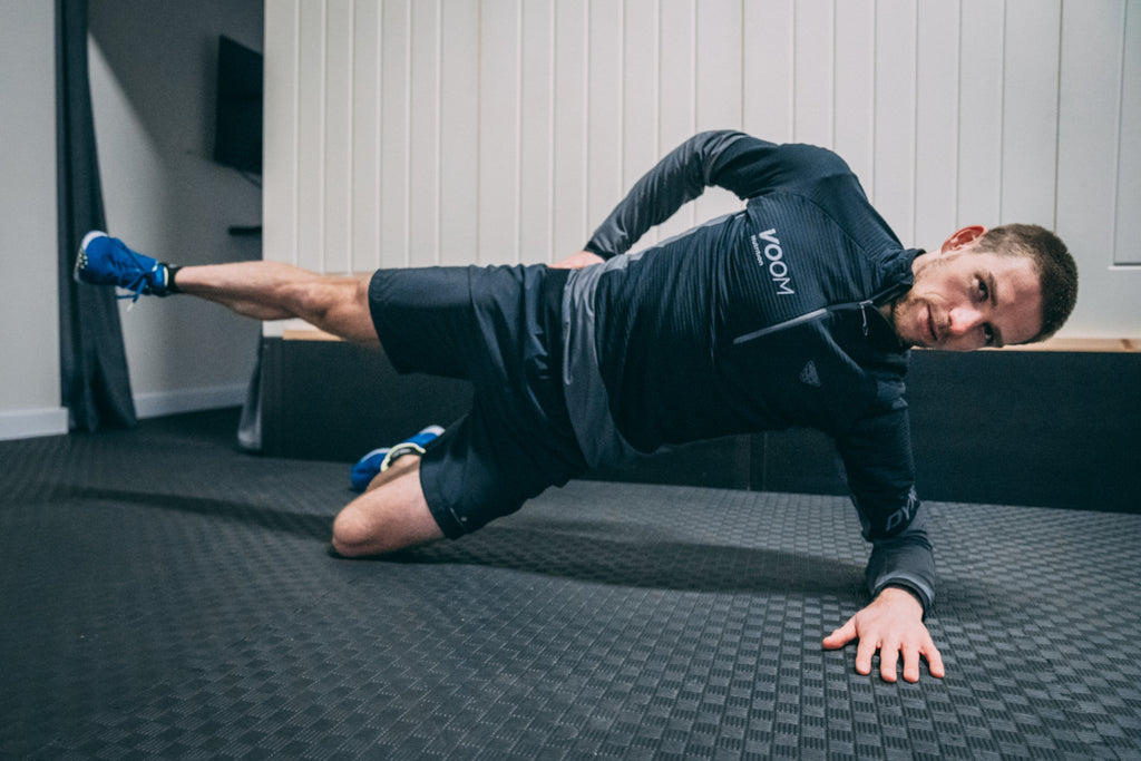 Male runner performs a side plank with leg raise to strengthen the glutes during an s&c for runners training session