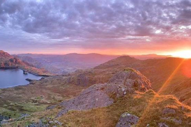 The sun rises with an orange sky above the stwlan dam in the moelwynion mountains of Snowdonia national park.